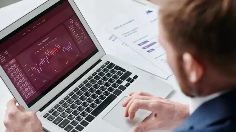 Businessman reviewing data analytics dashboard on laptop in bright office.